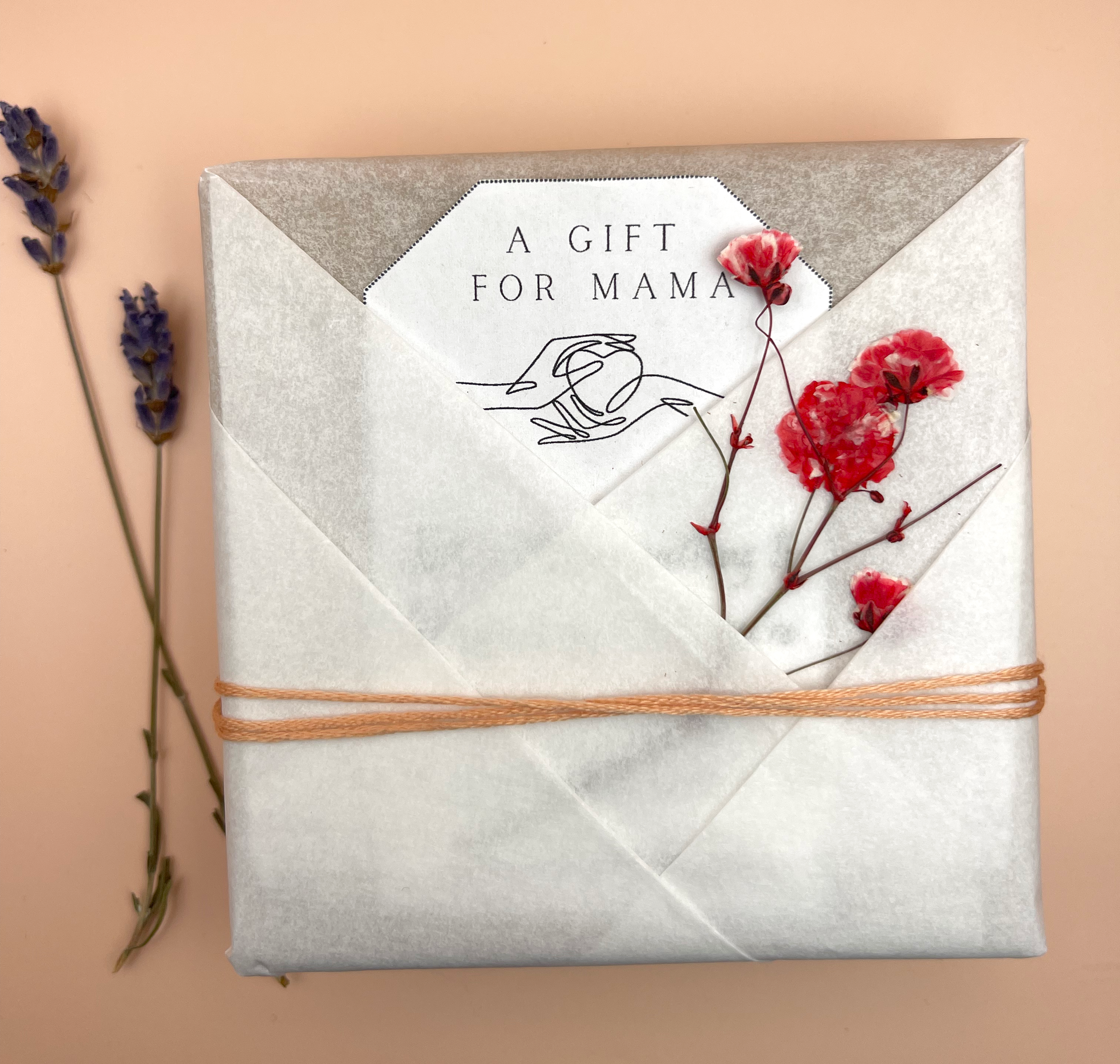 wrapped gift using unique fold technique and dried flowers. shows the option to include a personalized message.  the message card has a line drawn hand giving a hear to another hand.  on top, it reads 'a gift for mama' 
